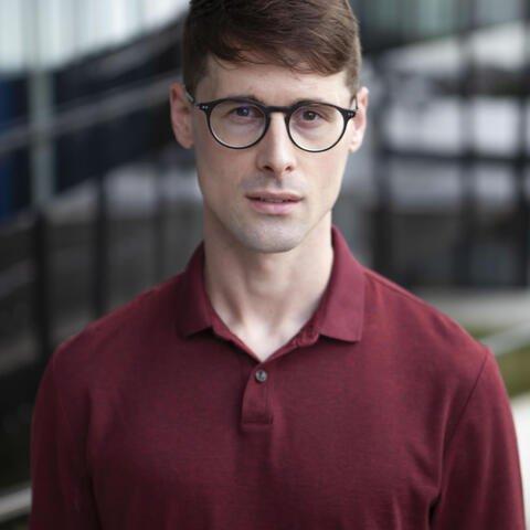 A person looking at the camera wearing a maroon shirt and glasses.